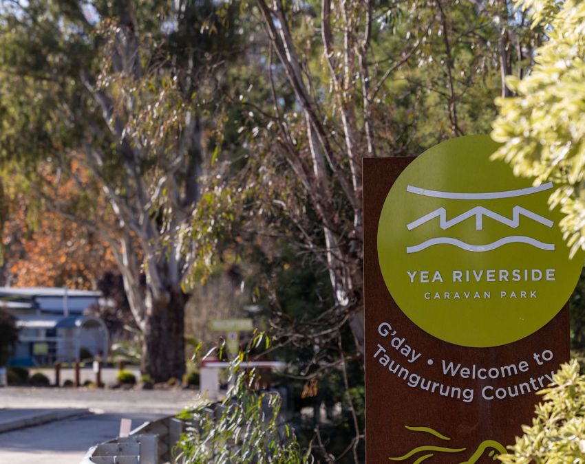 A long view looking own a bridge with the Yea Riverside Caravan Park front entrance and Welcome Sign in the foreground